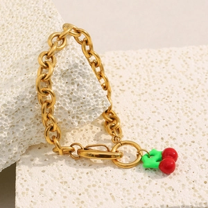 Detailed shot of gold-plated chunky chain bracelet with red cherry charm on white stone