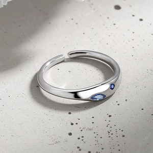 Minimalist silver stainless steel open ring with a blue diamond on concrete background