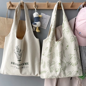 Detail of canvas tote bags featuring green leaf prints and artistic typography on hooks