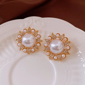 Détail de boucles d'oreilles fleur vintage avec perle centrale et strass brillants