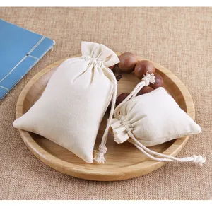 Set of two off-white canvas drawstring pouches in natural linen texture on a wood tray