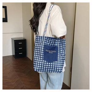 Detalle del bolso tote de lona a cuadros azules con correas trenzadas y bolsillo bordado