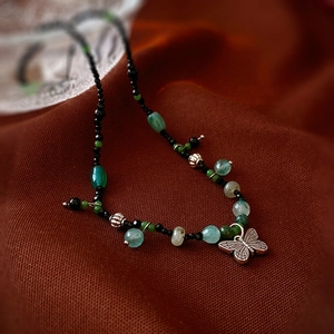 Detailed close-up of a vintage butterfly pendant with green gemstone beads on fabric