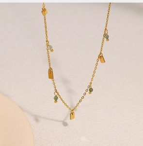 Detail of gold chain necklace featuring green round beads and rectangular pendants