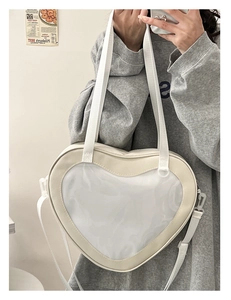 Detail of a beige heart-shaped ita bag with a clear PVC window and adjustable strap