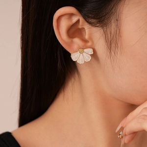 Close-up of elegant white flower stud earrings with gold trim worn by a model