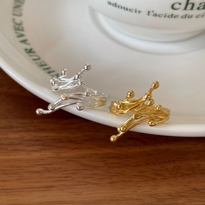 Macro shot of irregular branch-shaped gold and silver rings on a white porcelain dish