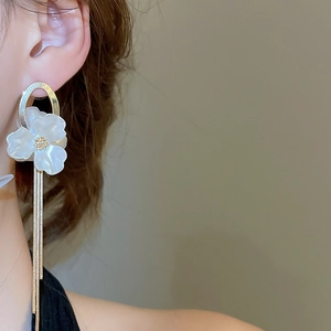 Elegant long gold fringe earrings with white shell flower details shown on a model