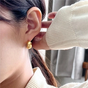 Minimalist matte gold U-shaped earring in bean design shown on a model with brushed texture