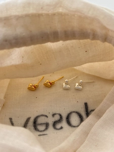 Close-up of gold and silver S925 sterling silver heart studs on linen fabric