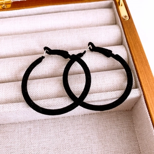 Detail shot of black flocked round hoop earrings resting in a beige linen jewelry box