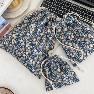 Three-piece set of navy floral drawstring pouches in various sizes on a white desk