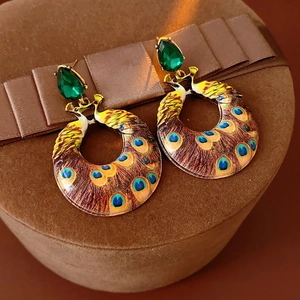 Macro detail of vintage enamel peacock earrings featuring green gems on a gift box lid