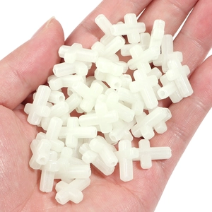 Luminous plastic cross beads for DIY jewelry making held in hand for scale and texture