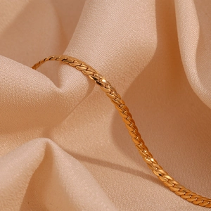 Detailed macro shot of 18K gold plated stainless steel curb chain on beige fabric