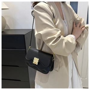 Détail d'un sac bandoulière noir avec fermoir ours doré porté sur un blazer beige chic