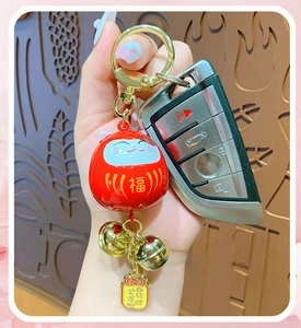 Close-up of red Daruma bell keychain with gold lucky charm held in hand over wood