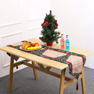 Detail of Christmas table runner with festive tree patterns and red tassels on wooden table