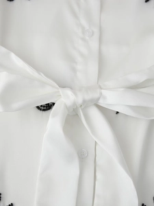 Detail of white blouse featuring black bead embroidery and elegant large bow tie decoration