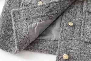 Détail de la texture du tweed gris et des boutons dorés gaufrés sur la veste courte