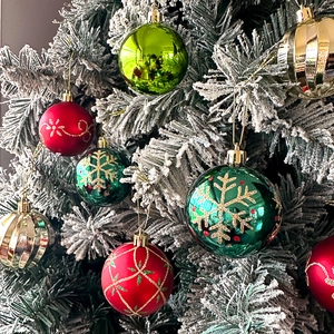 Close-up of red and green glittery Christmas baubles with snowflakes on snowy pine branch
