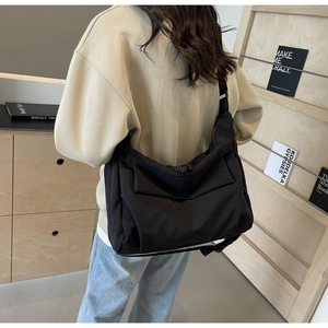 Rear view of a model wearing a large black nylon crossbody bag in a minimalist room