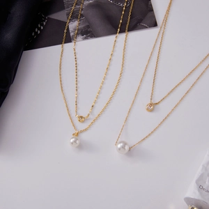 Détail de colliers dorés double épaisseur avec pendentifs perle et zircone
