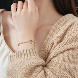 Close-up of a vintage gold chain bracelet with a purple enamel clover pendant on a wrist