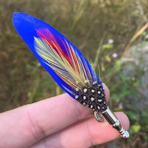 Detailed close-up of handmade peacock feather brooch with vibrant blue and red textures