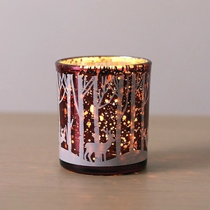 Close-up of a red glass candle holder with hollow forest and deer pattern with warm light