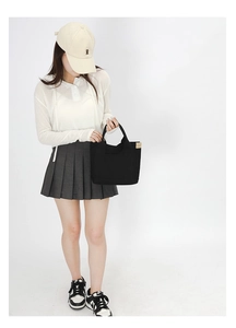 Full view of black canvas tote bag with dual handles worn by model in a studio setting