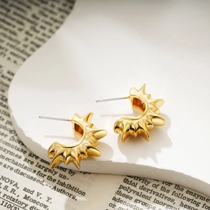 Macro shot of 18K gold sunburst C-shaped earrings on vintage newspaper background