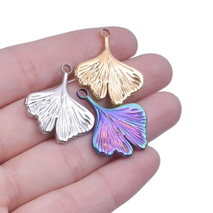 Macro shot of ginkgo leaf pendants in gold, silver, and rainbow finishes held by hand