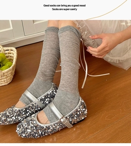 Detail of grey knitted ballet style calf socks with silver Mary Jane shoes on wood floor
