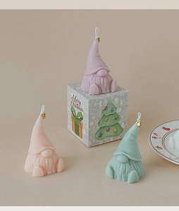 Close-up of three colorful Santa gnome scented candles with gold bells and gift boxes