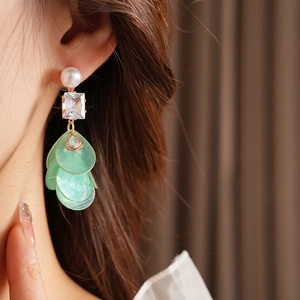 Nahaufnahme von Zirkon-Ohrringen mit Muschelblättern und Perlen an einem Modell mit Goldschmuck
