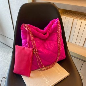 Magenta quilted puffer tote bag with chain strap and matching small pouch on a black chair