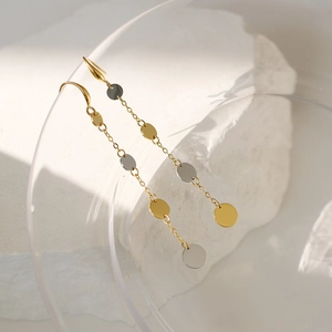 Detail of two-tone gold and silver circular drop earrings hanging on glass with stone backdrop