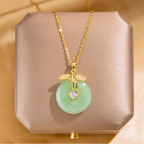 Macro shot of gold leaf pendant with green gemstone on champagne jewelry box