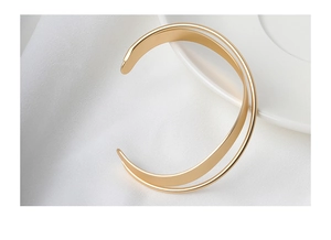 Dettaglio macro di un bracciale aperto incrociato minimalista con finitura in oro opaco