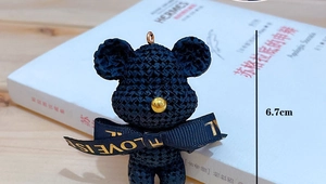 Detail of hand-woven black bear keychain with golden bead nose and blue bow ribbon