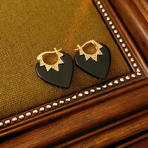 Detail of heart-shaped gold plated earrings with black enamel and star motif crystals