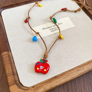 Gros plan du pendentif pomme rouge avec breloques colorées sur un collier en cordon tressé