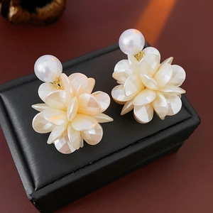 Détail de boucles d'oreilles fleurs en acrylique crème avec perles sur écrin noir