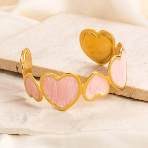 Close-up of golden bangle featuring pink enamel heart charms on a textured stone base