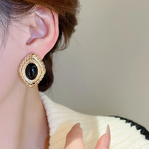 Detail shot of vintage gold scallop-edged stud earrings with oval black stones on ear