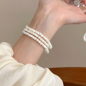 Elegant three-layer white beaded pearl bracelet styled on a woman's wrist with silk sleeve