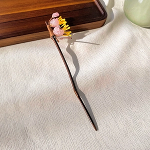 Detail of wooden hair stick featuring a delicate pink flower and yellow stamens