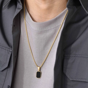 Close-up of minimalist men's gold chain with a black rectangular pendant on a model