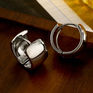 Polished silver huggie hoop earrings with snap closure on a rustic wood surface